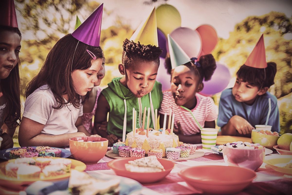 Cute children blowing together on the candle during a birthday party on a park 